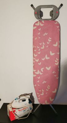 a ironing board with a pink cover and a pair of shoes next to it