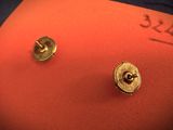 a pair of gold stud earrings sitting on a red pillow