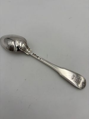 une cuillère ancienne en argent dont le manche repose sur une surface blanche