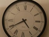 une horloge en noir et blanc accrochée au mur, avec des chiffres romains