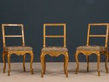 pair of gilded chairs with upholstered seats against a blue wall