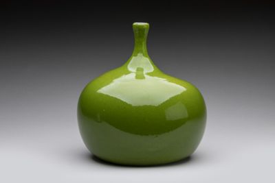 un vase vert posé sur une surface blanche, avec un fond gris