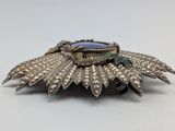 a close up of a silver broochle with a blue stone in the center