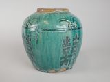 a green vase with writing on it sitting on a white surface
