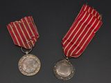 two medals on a black surface with a red and white striped ribbon