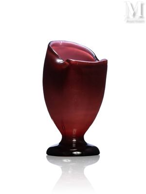 un vase rouge avec un socle noir posé sur une surface blanche