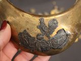 a woman holding a brass collar with a design on it