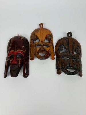 trois masques en bois accrochés à un mur sur un fond blanc