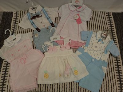 de nombreux vêtements de bébé étalés sur une couverture posée sur un lit