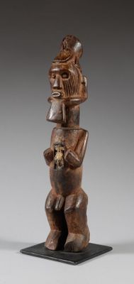 une statue en bois représentant un homme tenant un chat, posée sur un socle noir