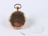 a gold pocket watch sitting next to a glass of water