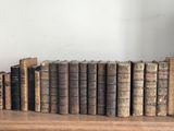 many old books on a shelf with a clock above them