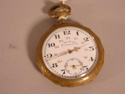 une montre à gousset en or suspendue à un mur blanc