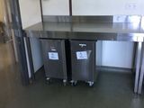 two stainless steel tables in a kitchen with two trash cans