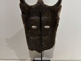 a close up of a wooden mask on a stand on a white surface