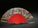a red fan with a painting on it sitting on a table