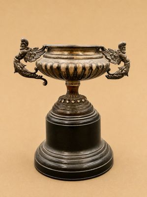 un vase en argent orné de deux oiseaux, posé sur un socle