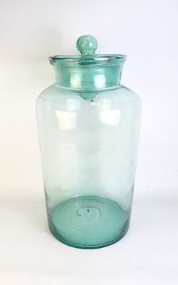 un bocal en verre vert muni d'un couvercle, posé sur une surface blanche