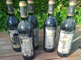 six bottles of wine sitting on a wooden table in front of a bush