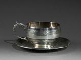une tasse et une soucoupe anciennes en argent, posées sur un plateau en argent