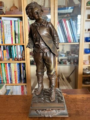 une statue en bronze représentant un garçon debout sur une table