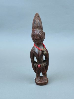 une vieille figurine en bois représentant un homme avec un ruban rouge autour du cou