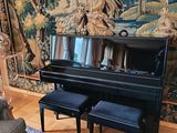 un piano noir dans un salon où une tapisserie est accrochée au mur