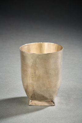 silver cup sitting on a table with a shadow on the ground