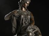 bronze statue of a woman sitting on a stool with her hands on her knees