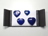 quatre boutons bleus en forme de cœur dans une boîte noire posée sur une surface blanche