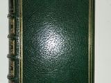 an old green book with gold trim sitting on top of a white table