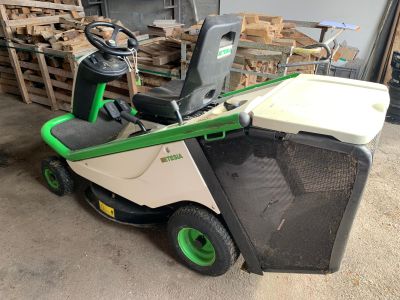 a green and white lawn mower parked in front of a pile of wood