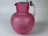pichet en verre rose avec une anse argentée sur un fond blanc
