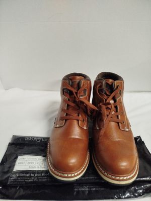 une paire de bottes en cuir marron posées sur un sac noir, lui-même posé sur une surface blanche