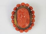 an image of a coral and gold broochle with a carved face on it