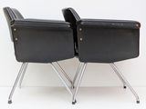 pair of black leather chairs with chrome legs against a white wall