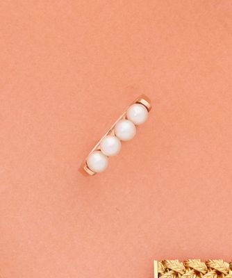 un gros plan d'une bague en or ornée de perles sur fond rose