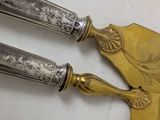 two silver spoons on a white table with a gold handle