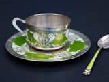 une tasse et une cuillère en argent posées sur une assiette verte