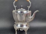 an antique silver tea pot on a stand with a wooden handle