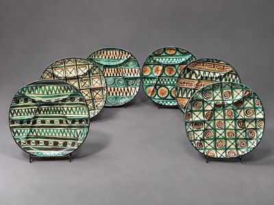 cinq assiettes vertes et marron ornées de motifs, posées sur une surface grise