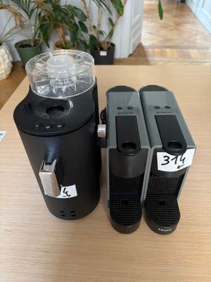 two black coffee machines sitting on top of a table next to a plant