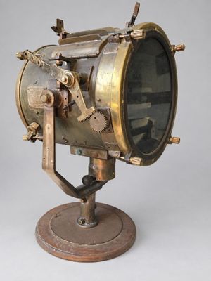 une lampe en laiton à l'ancienne, posée sur un socle en bois, sur fond gris