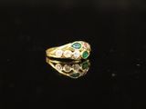 a gold ring with emerald and white diamonds on a black surface