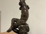 statue of a man sitting on a rock with a spear in his hand