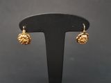 a pair of gold toned earrings on a black stand