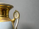 a gold vase with a painting on it sitting on a table