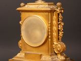 a gold clock sitting on a wooden table with a black background