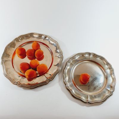 two silver plates with oranges in them on a white table