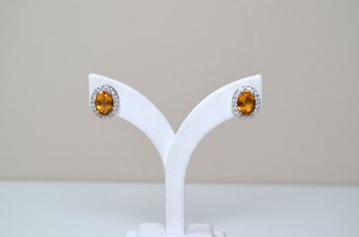 une paire de boucles d'oreilles ornées de pierres orange, posée sur un support blanc sur une table
